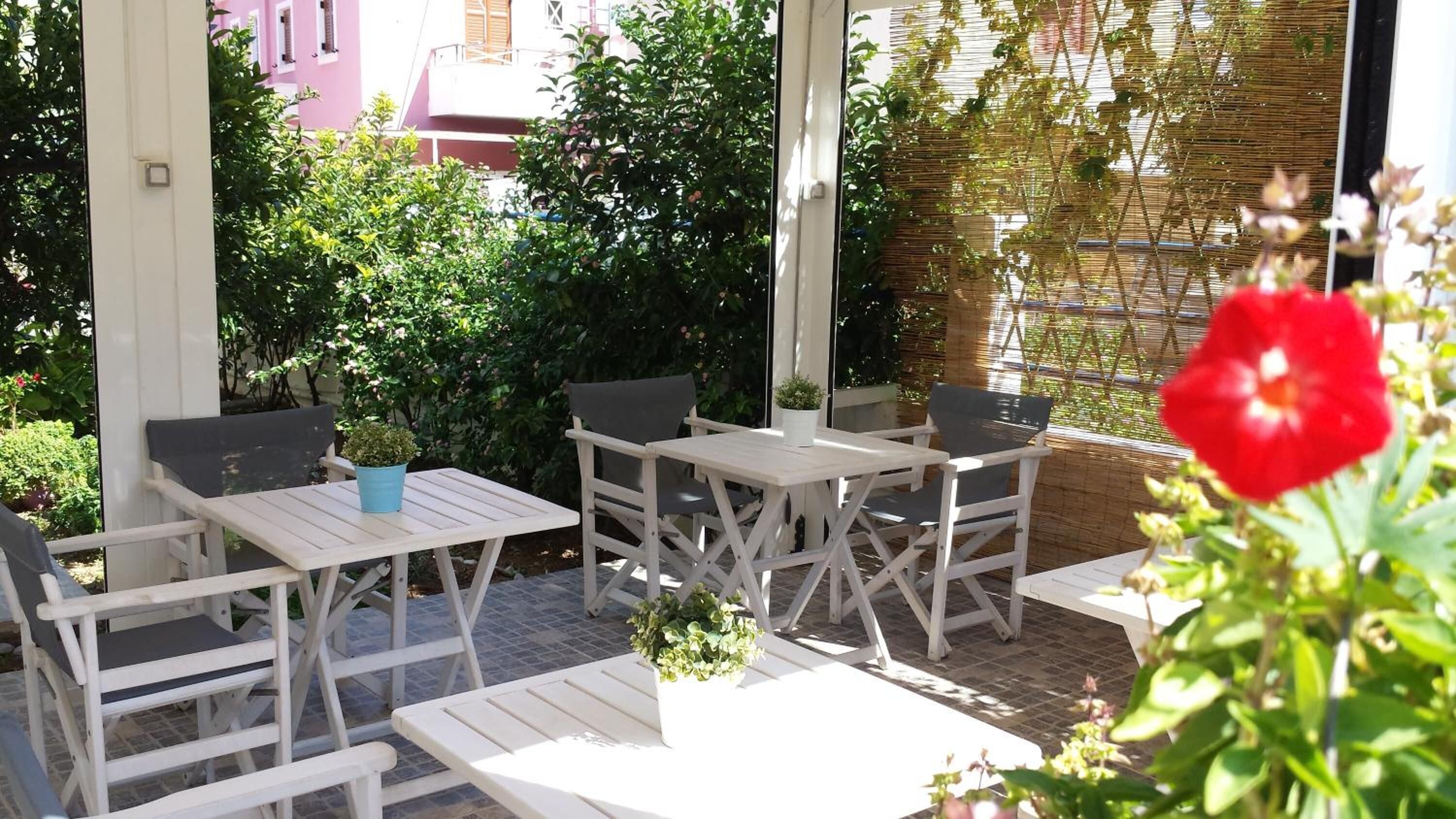 Een terras buiten met witte houten meubels, zoals tafels en stoelen, omgeven door weelderige begroeiing en een bamboe schutting.