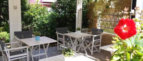 Een terras buiten met witte houten meubels, zoals tafels en stoelen, omgeven door weelderige begroeiing en een bamboe schutting.