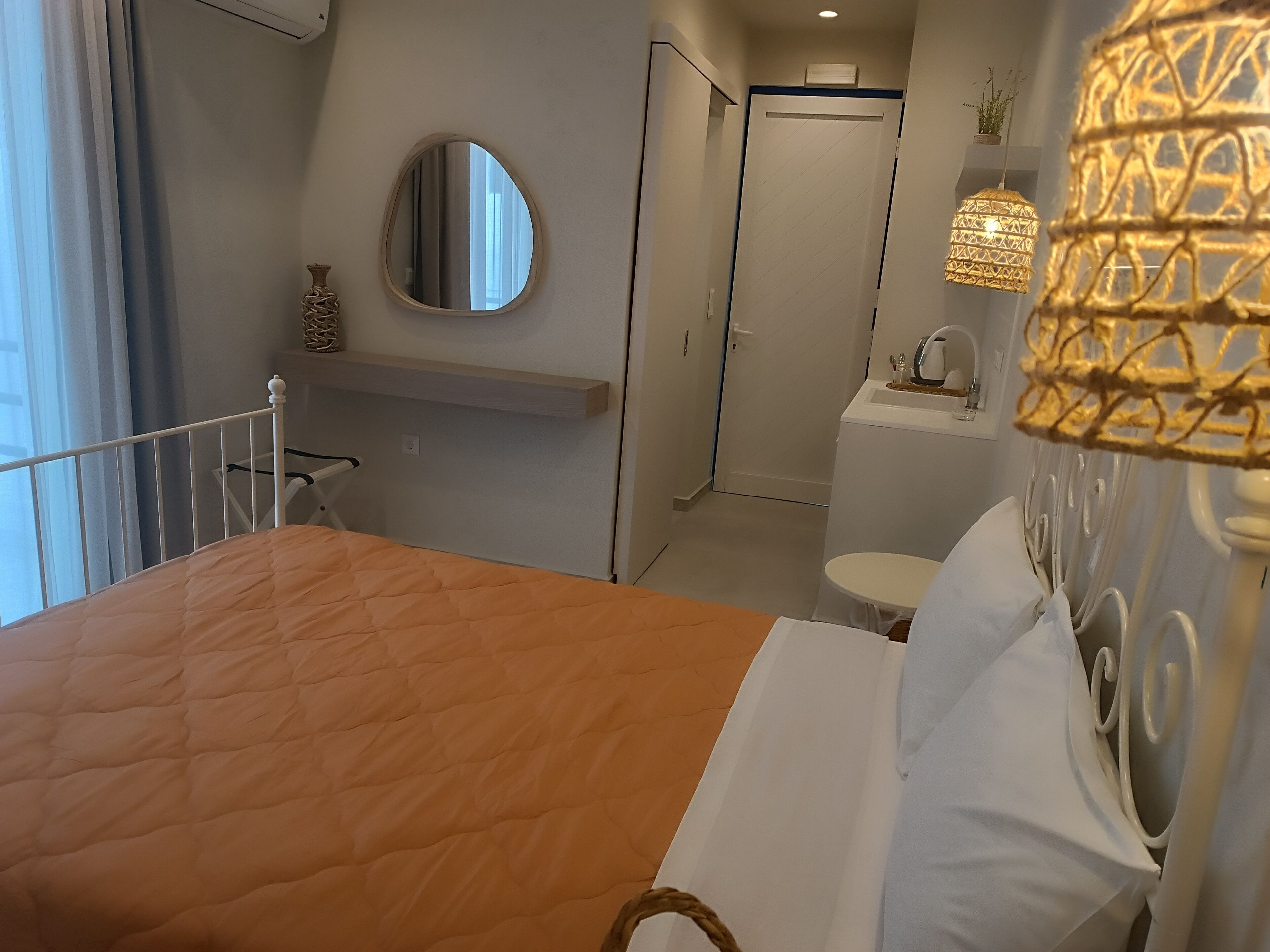 A hotel room with a bed, a bedside table, a mirror, a toilet, and a sink.
