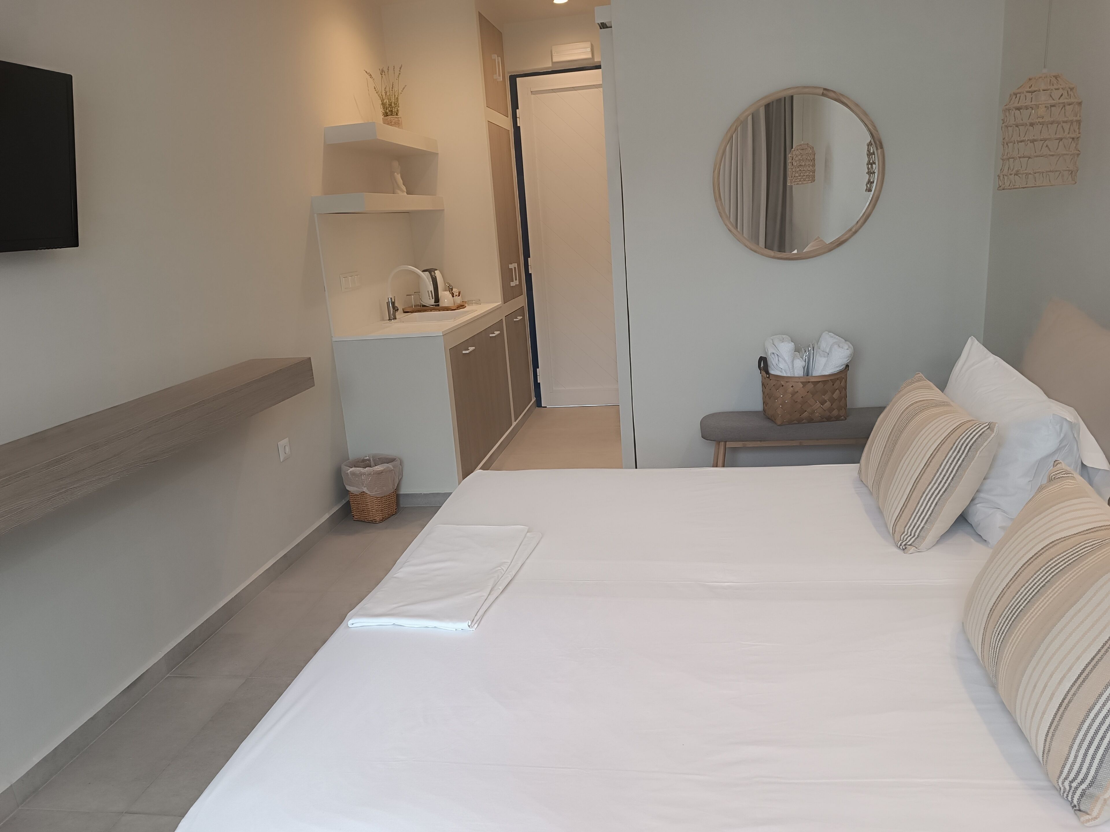 A modern hotel room with a large bed, a small seating area, a bathroom, and a TV mounted on the wall.