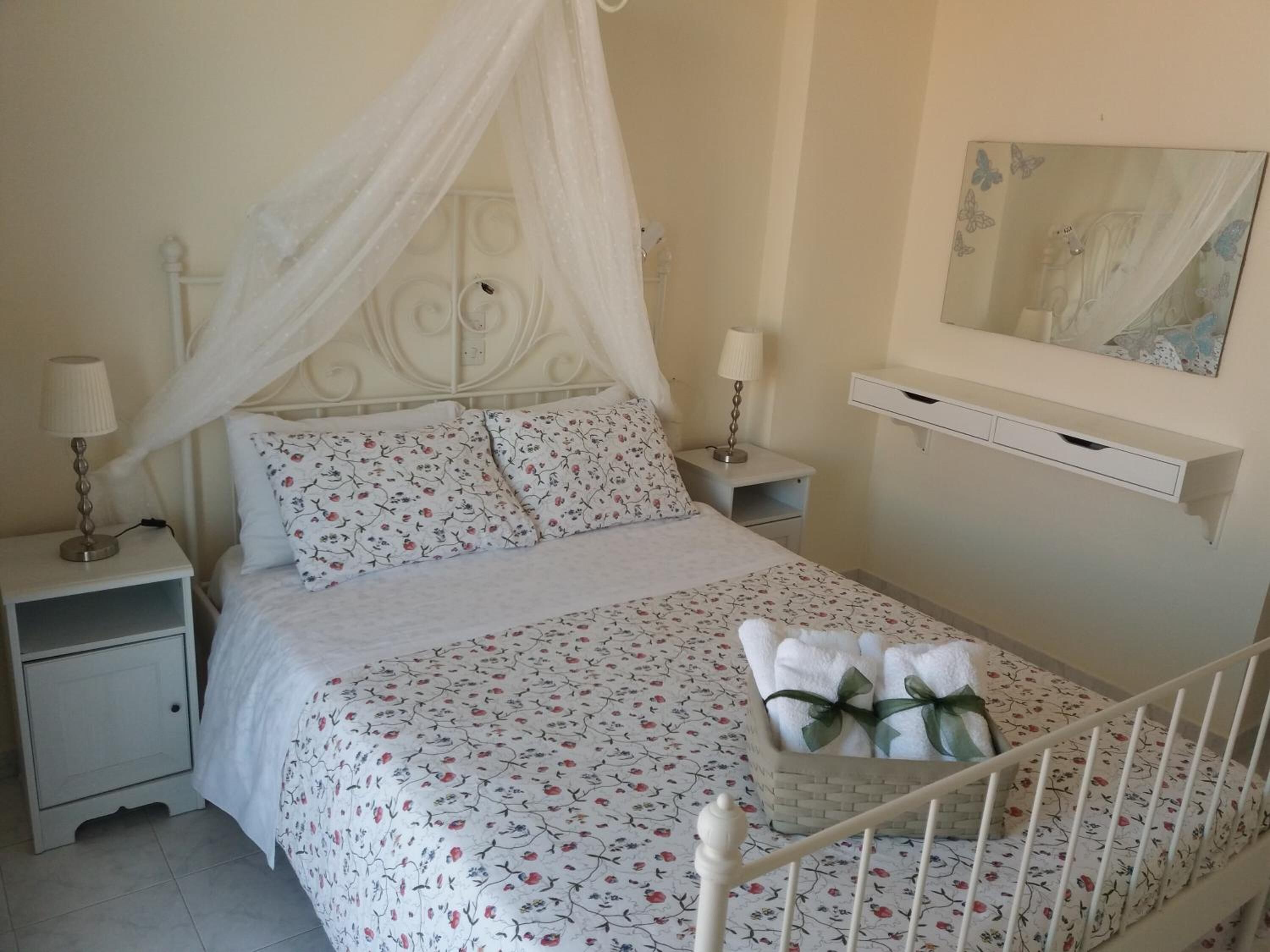 A neatly made bed with a floral bedspread, a white canopy, and a bedside table with a lamp.