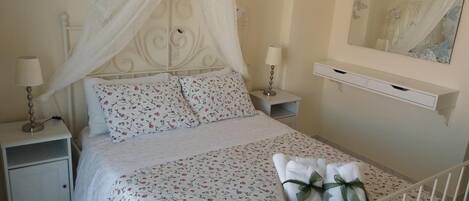 A neatly made bed with a floral bedspread, a white canopy, and a bedside table with a lamp.