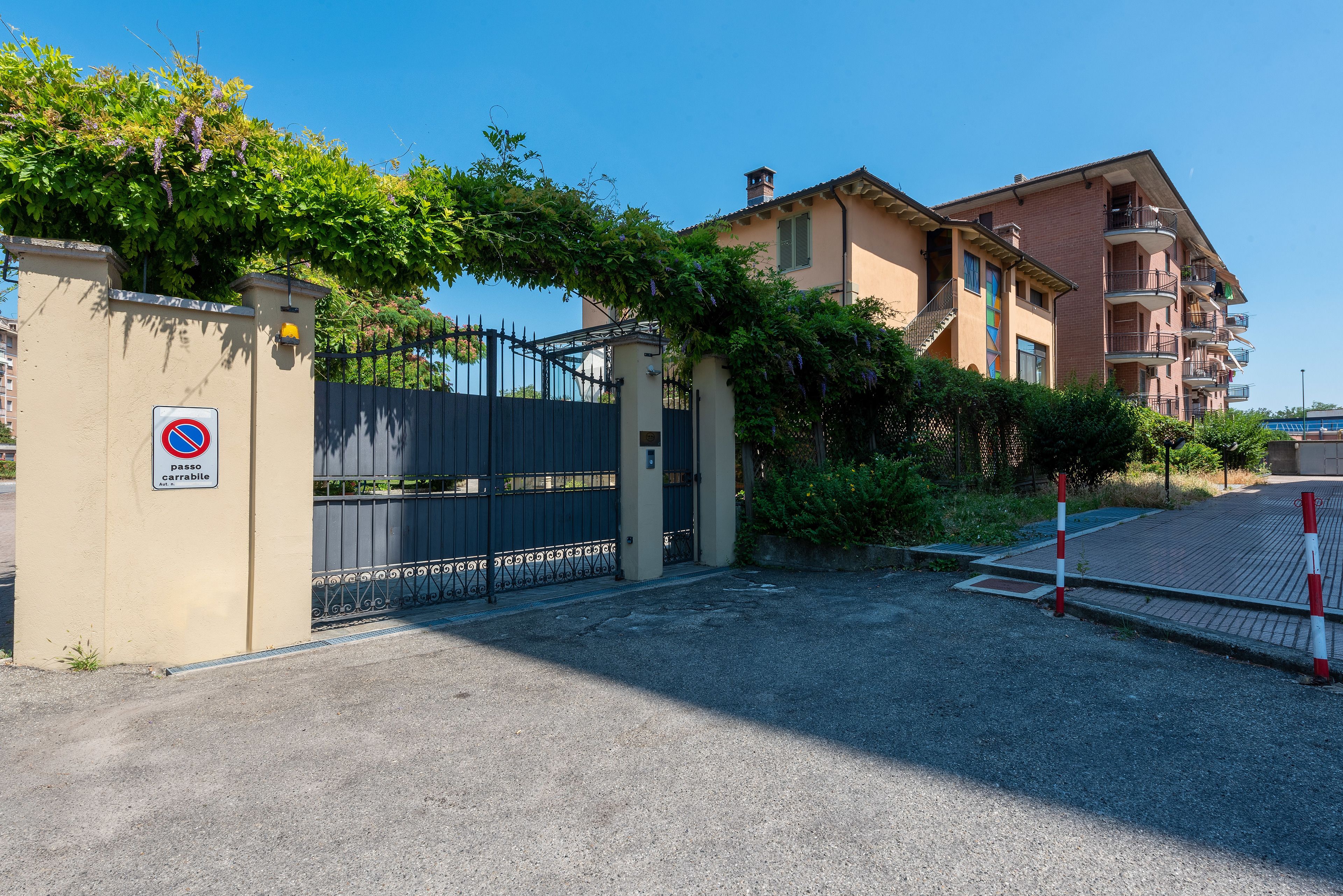 A gated entrance to a residential building with a no parking sign, a metal gate, and a clear sky.