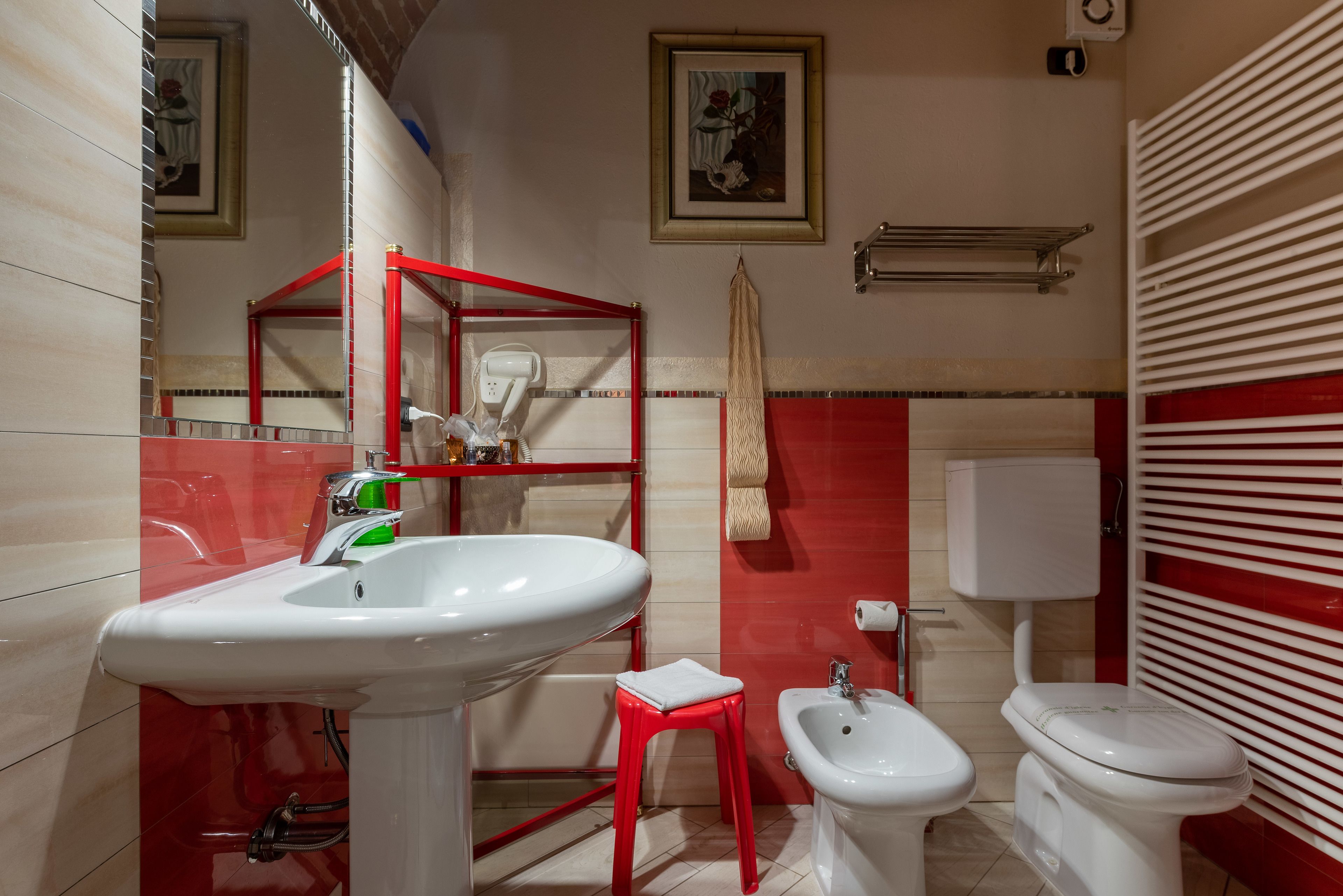 Ein Badezimmer mit Waschbecken, rotem Hocker, Bidet, Toilette und Handtuchhalter.