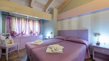 A bedroom with two beds, wooden ceiling beams, a window with purple curtains, and a bedside table with a lamp.