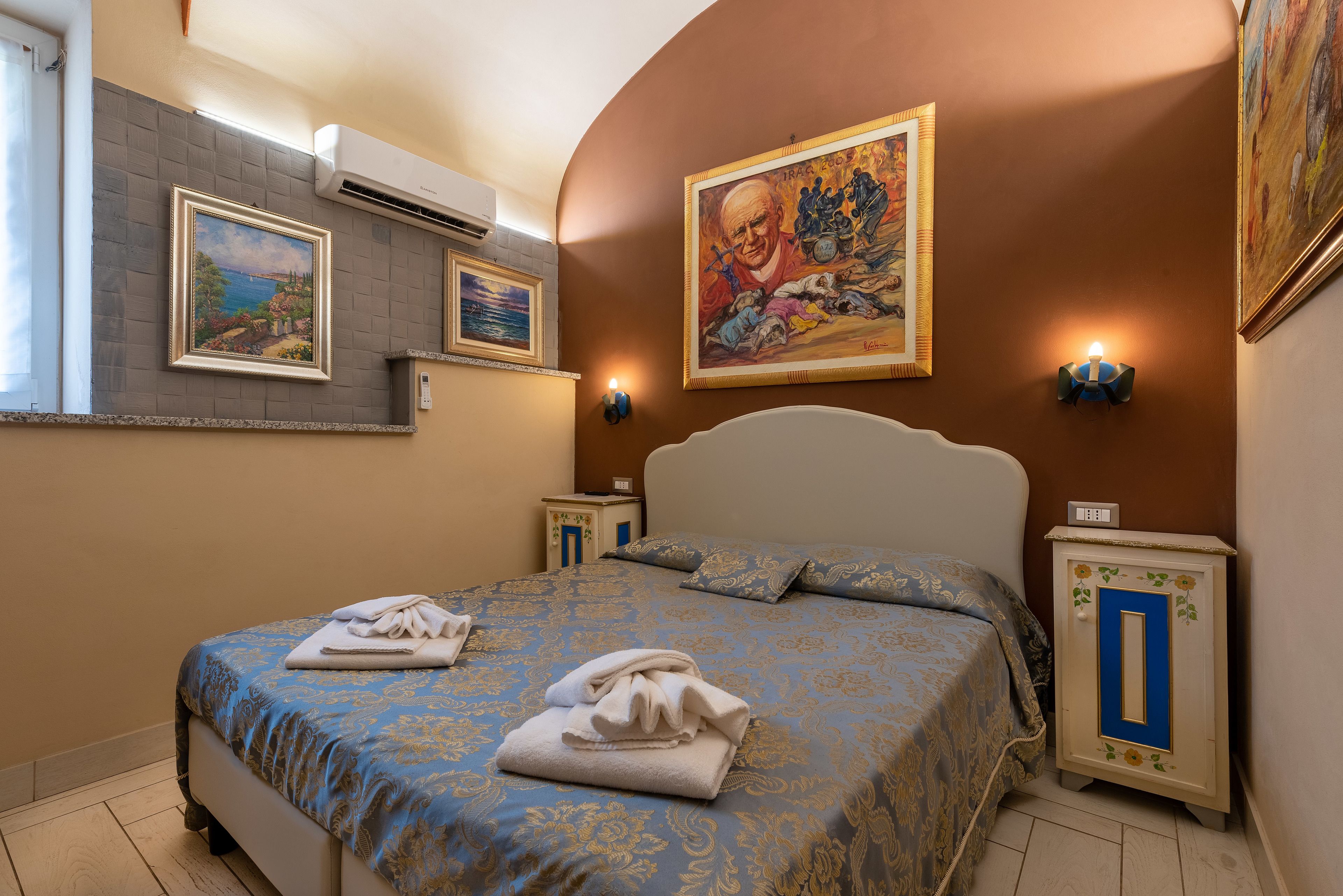 Um quarto com cama, mesa de cabeceira, ar condicionado fixado na parede e um quadro.