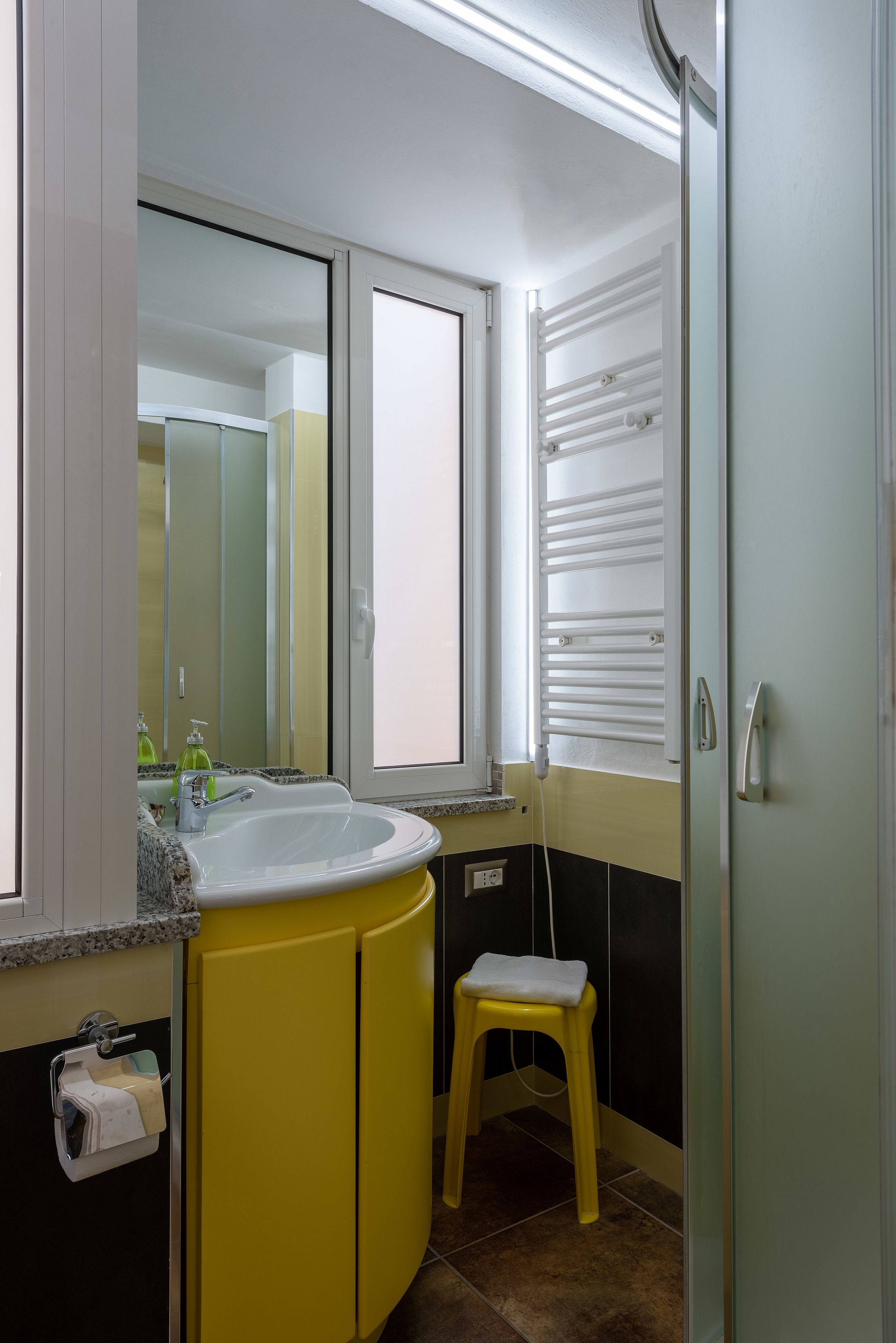 Een badkamer met een geel wastafel, een spiegel, een raam en een handdoekhouder.