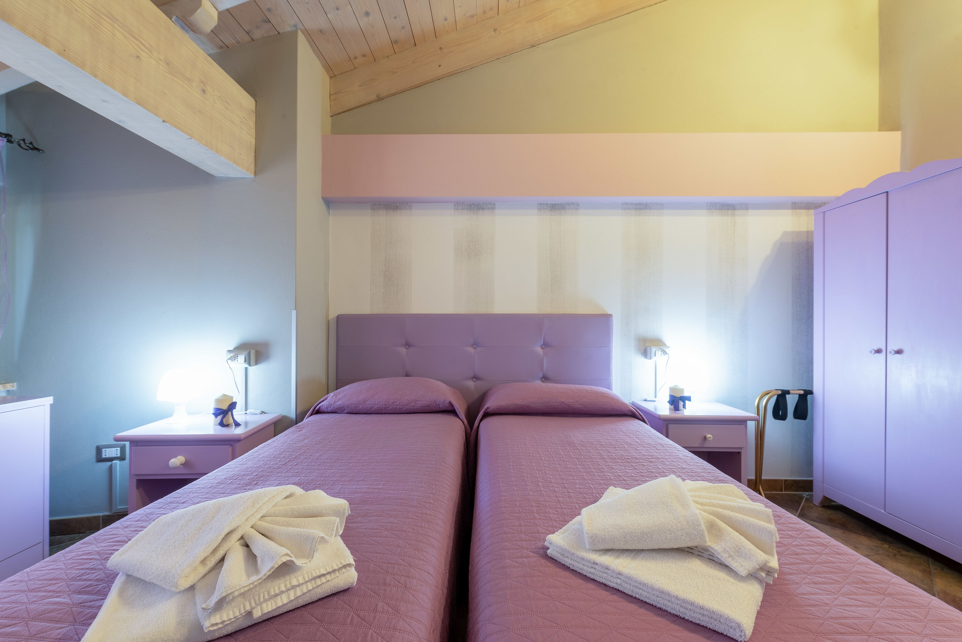 Un dormitorio con dos camas, un armario y una mesita de noche con una lámpara.