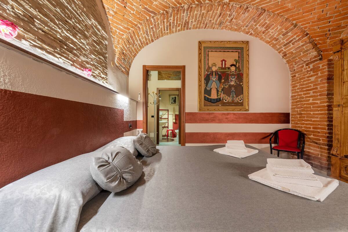 Une chambre d’hôtel avec une arche en briques, un lit avec des oreillers, un fauteuil rouge et un tableau accroché au mur.