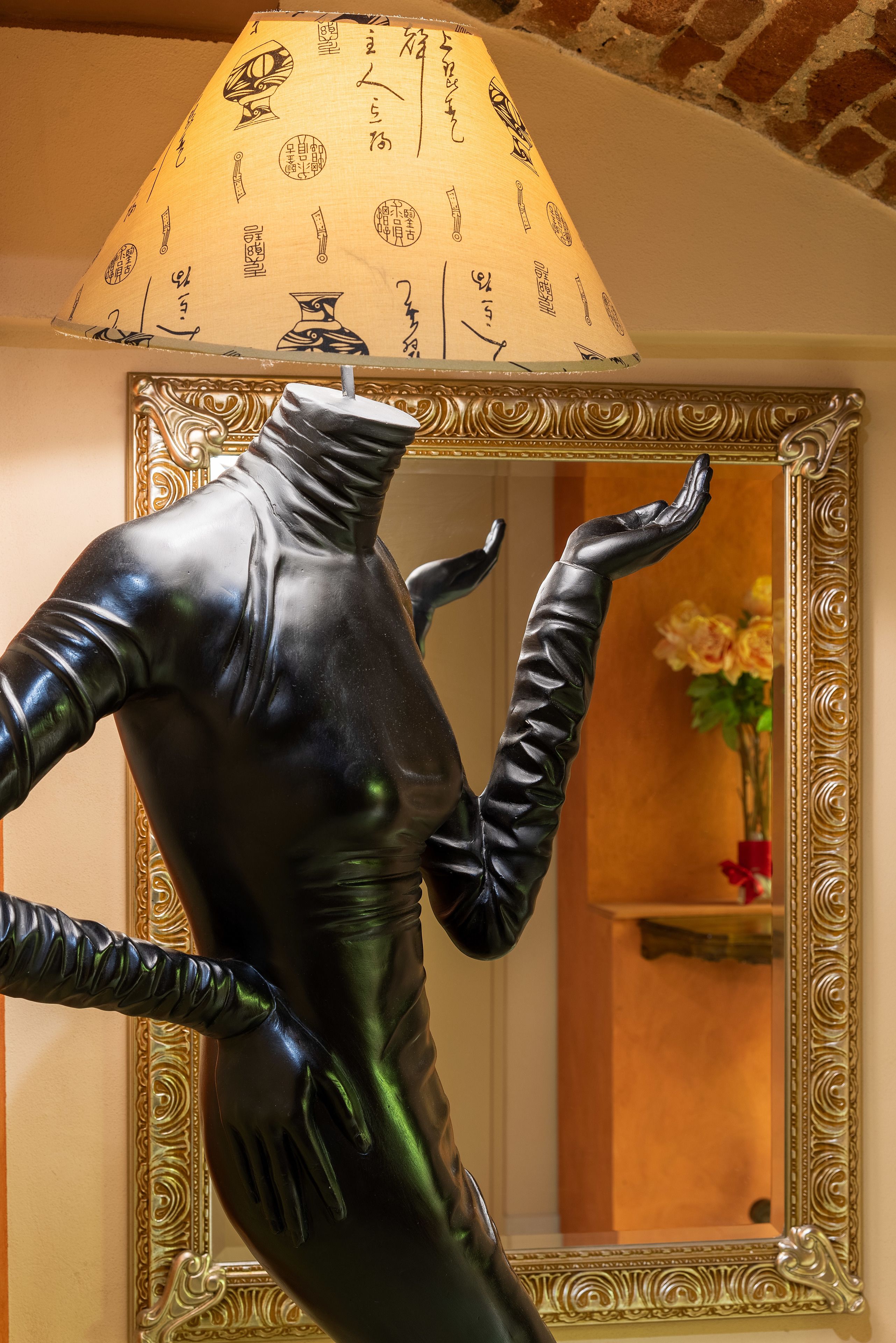 Una estatua de una figura con los brazos extendidos y una superficie reflectante frente a un espejo ornamentado con un marco decorativo.