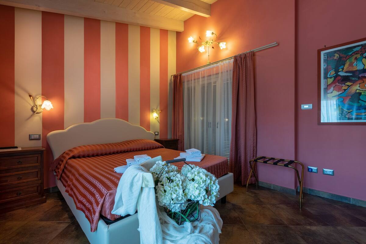 Une chambre à coucher comprenant un lit, une table de chevet, une commode, une fenêtre avec des rideaux et un luminaire fixé au mur.