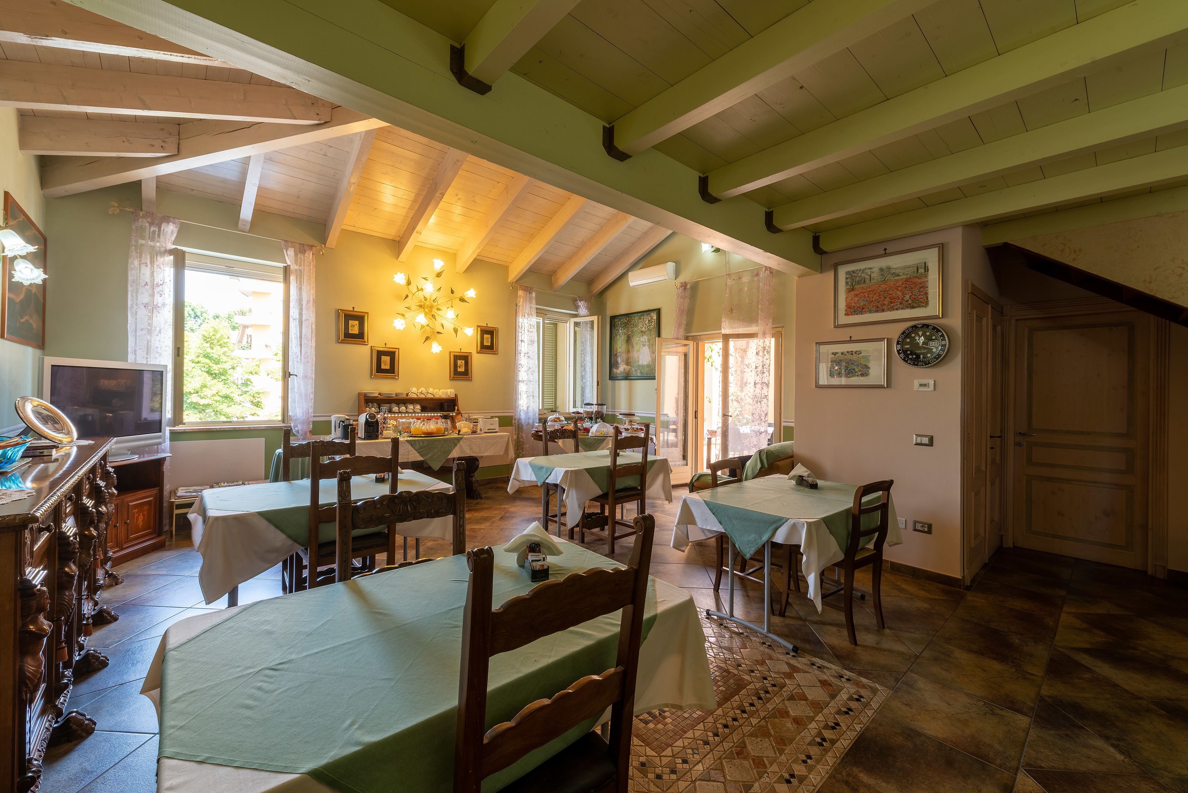 A dining area with multiple tables and chairs, wooden beams on the ceiling, and a chandelier.