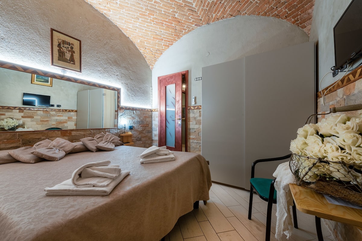 Une chambre d’hôtel avec un lit, des serviettes, un miroir, une télévision et un mur en briques.