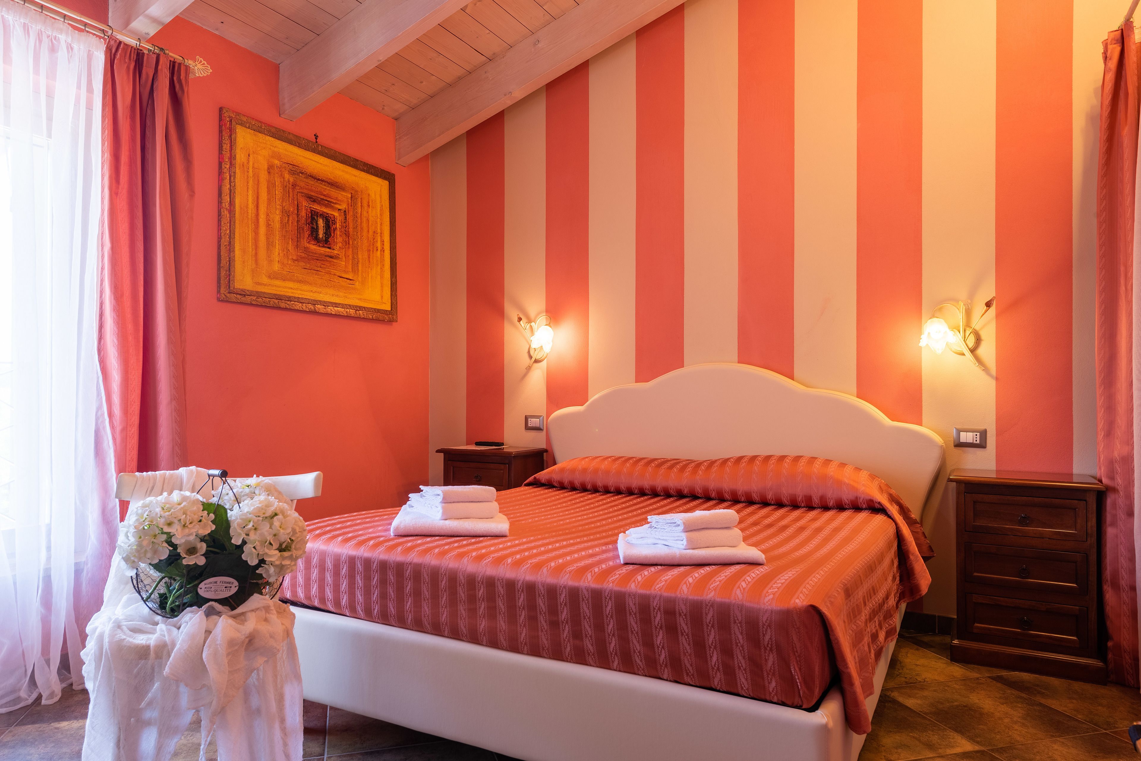 Une chambre d’hôtel avec un mur à rayures, un lit avec une literie blanche, deux tables de chevet et une petite table de nuit.