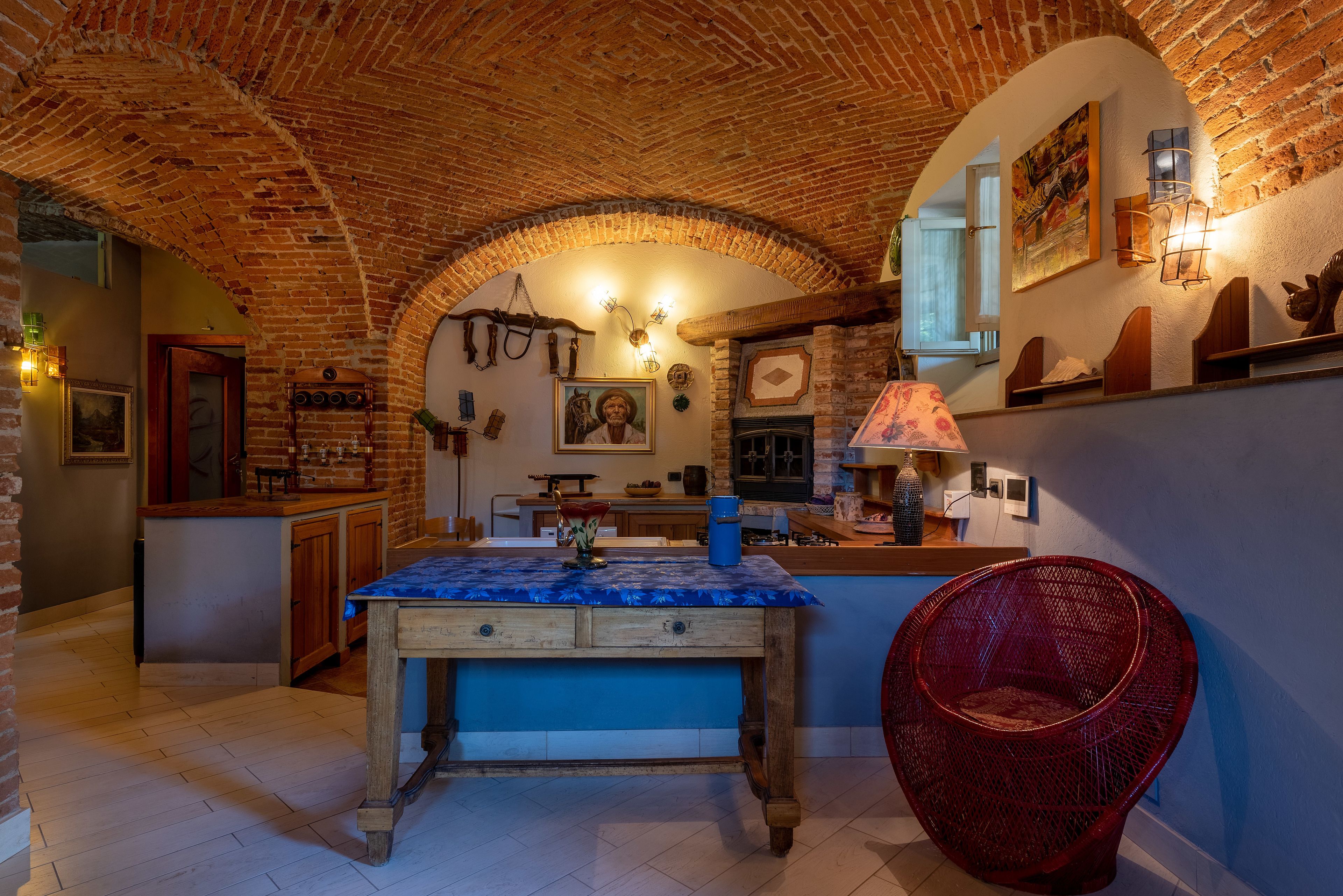 A rustic kitchen with exposed brick walls, a wooden table, and a red woven chair.
