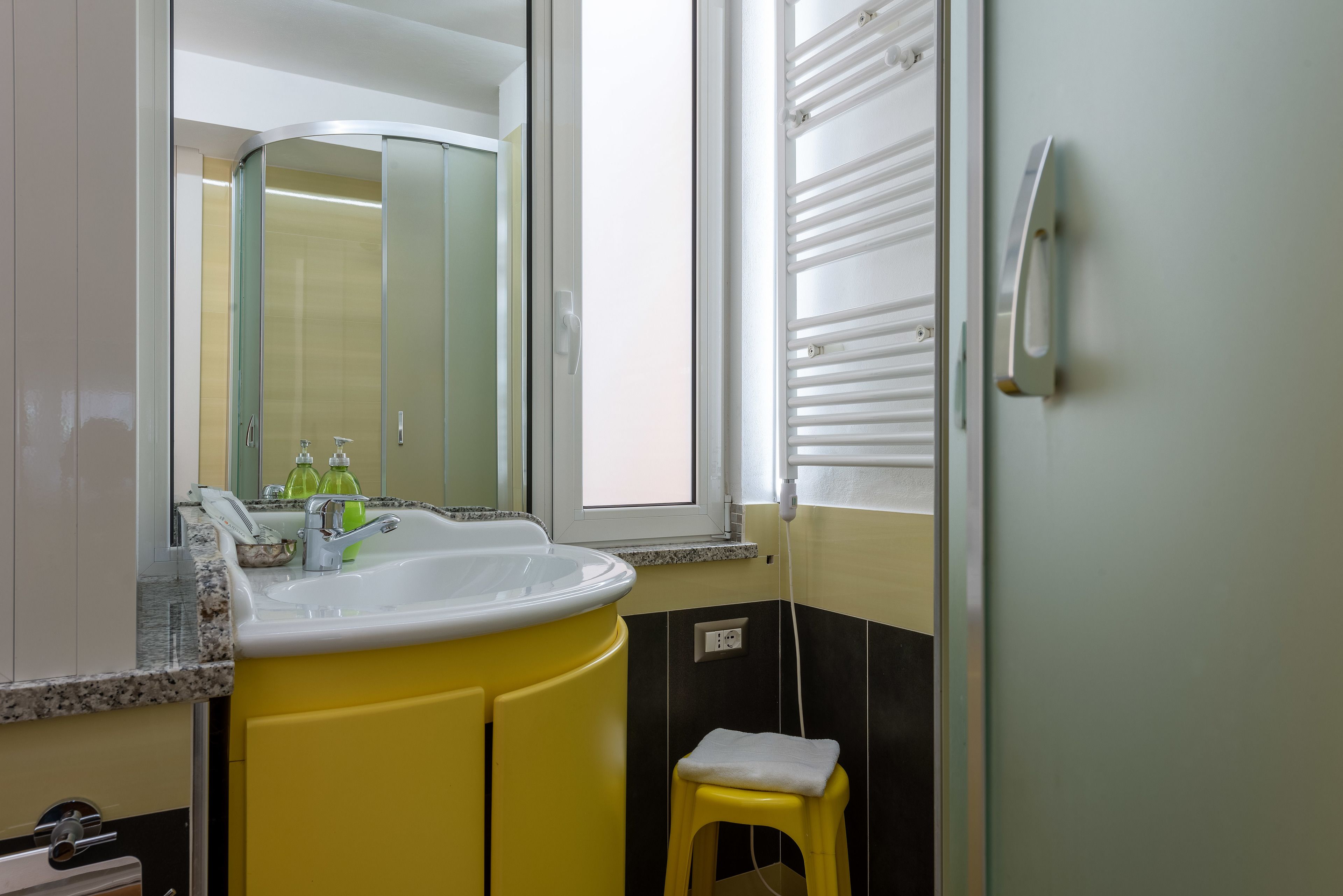 Ein Badezimmer mit einem gelben Waschbecken, einem Spiegel und einem Fenster.