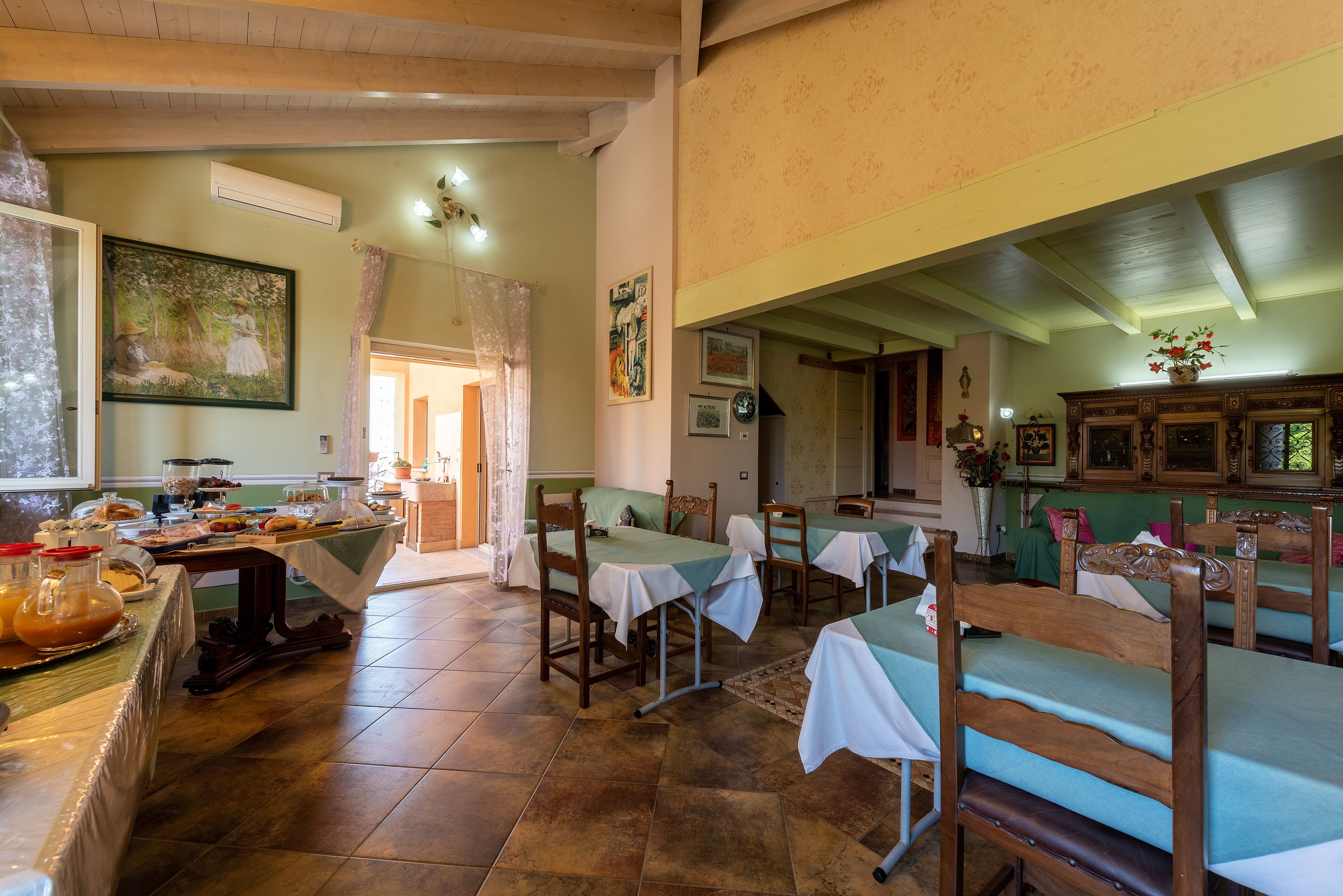 Un comedor con mesas preparadas para el servicio, un bufé con comida y bebidas, y un cuadro en la pared.