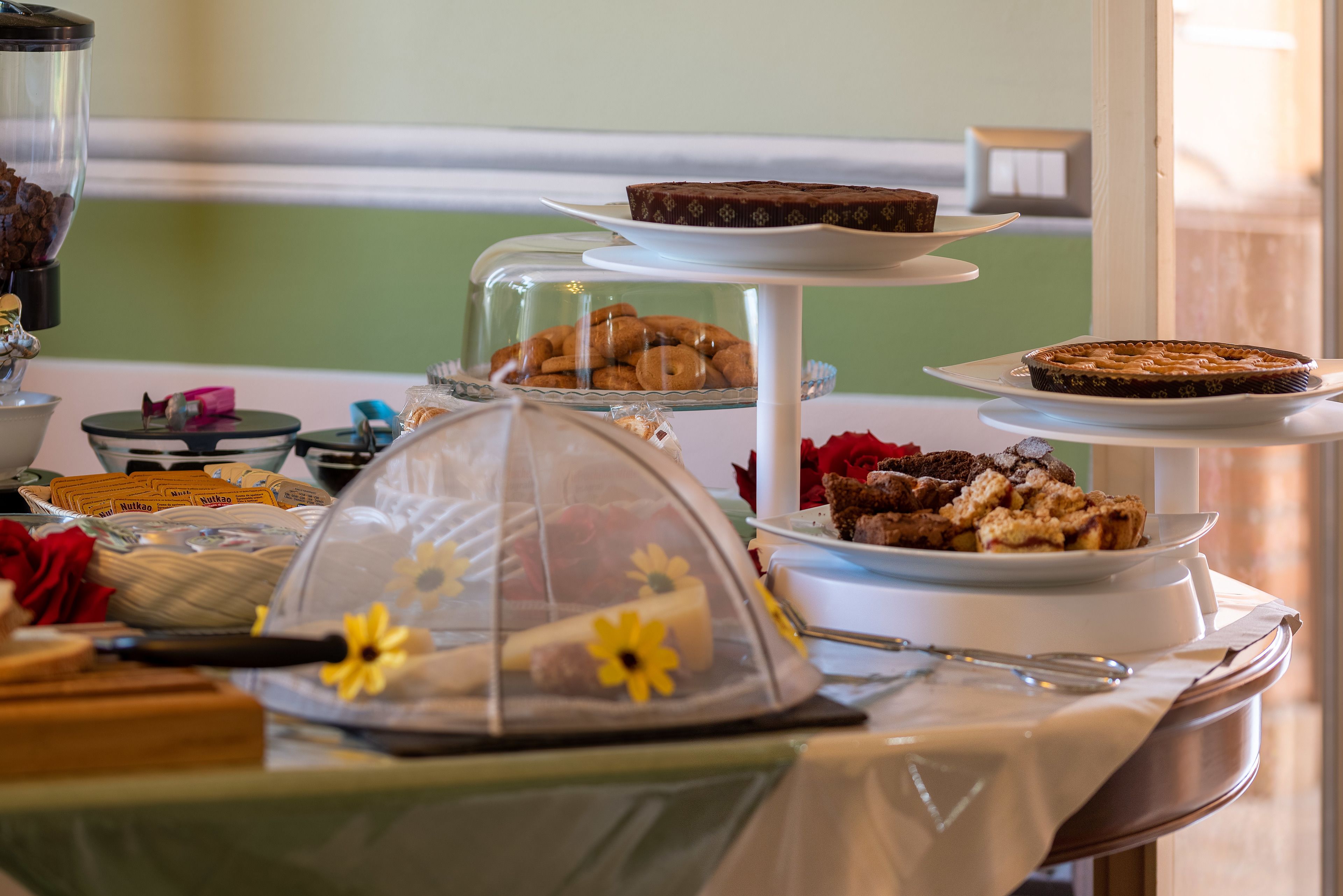 A buffet with various food items, including pastries, cakes, and a covered display case with flowers.