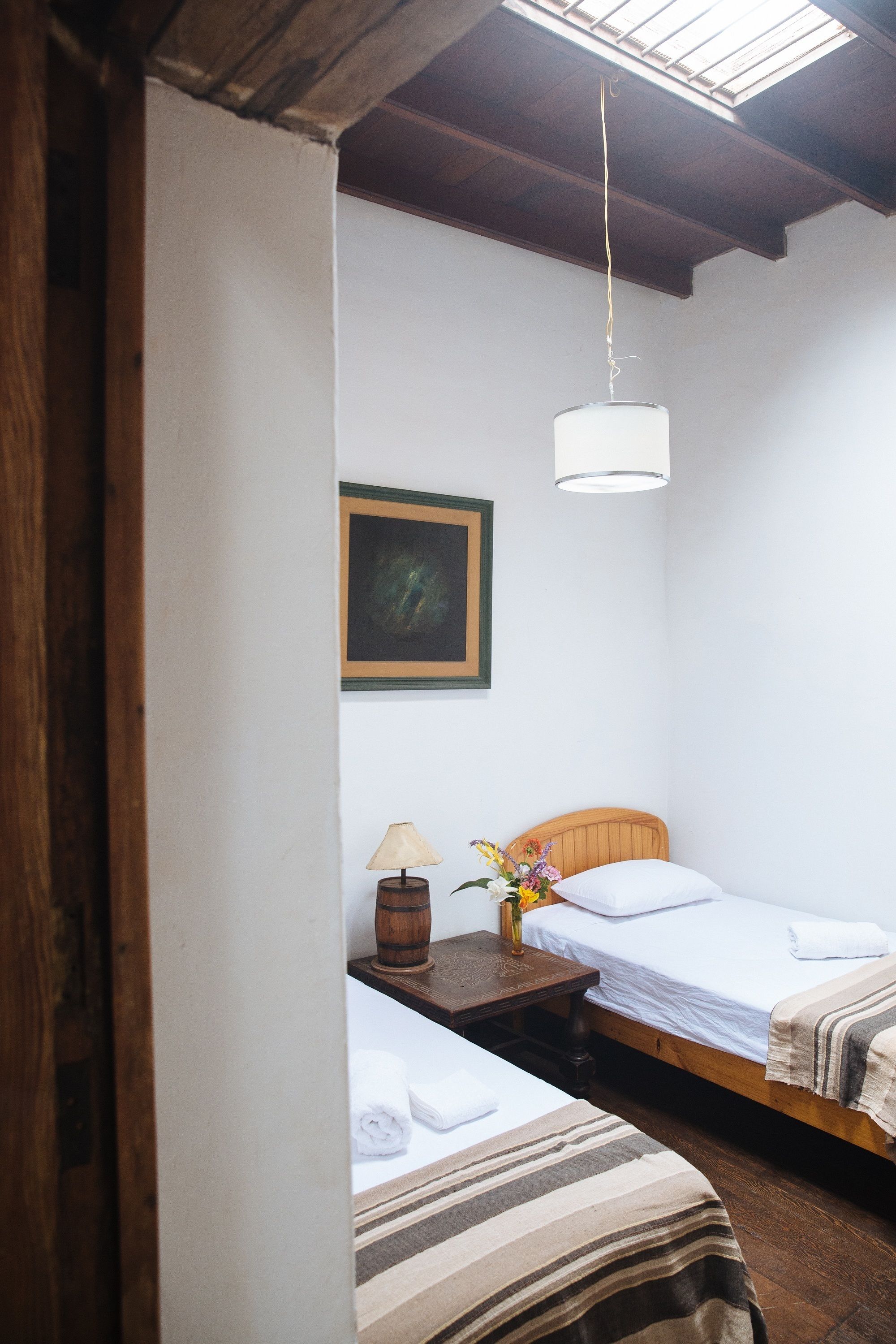 Una habitación pequeña y acogedora con dos camas, un cabecero de madera, una mesita de noche con lámpara y un cuadro en la pared.