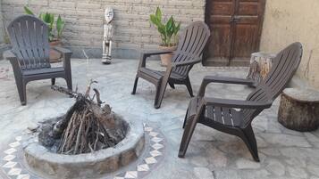 A patio area with four chairs, a small fire pit, and two potted plants.