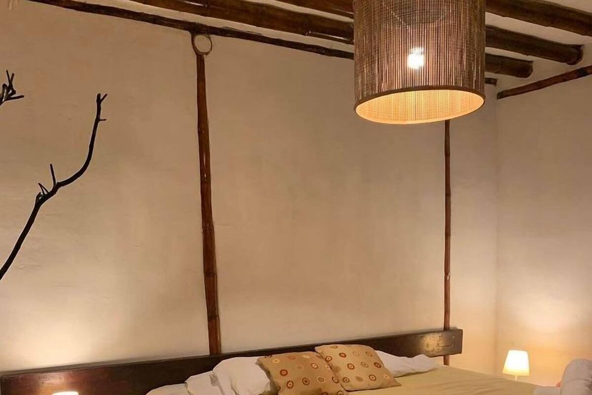 Una cama bien hecha con cabecera, dos lámparas de noche y una lámpara colgante.
