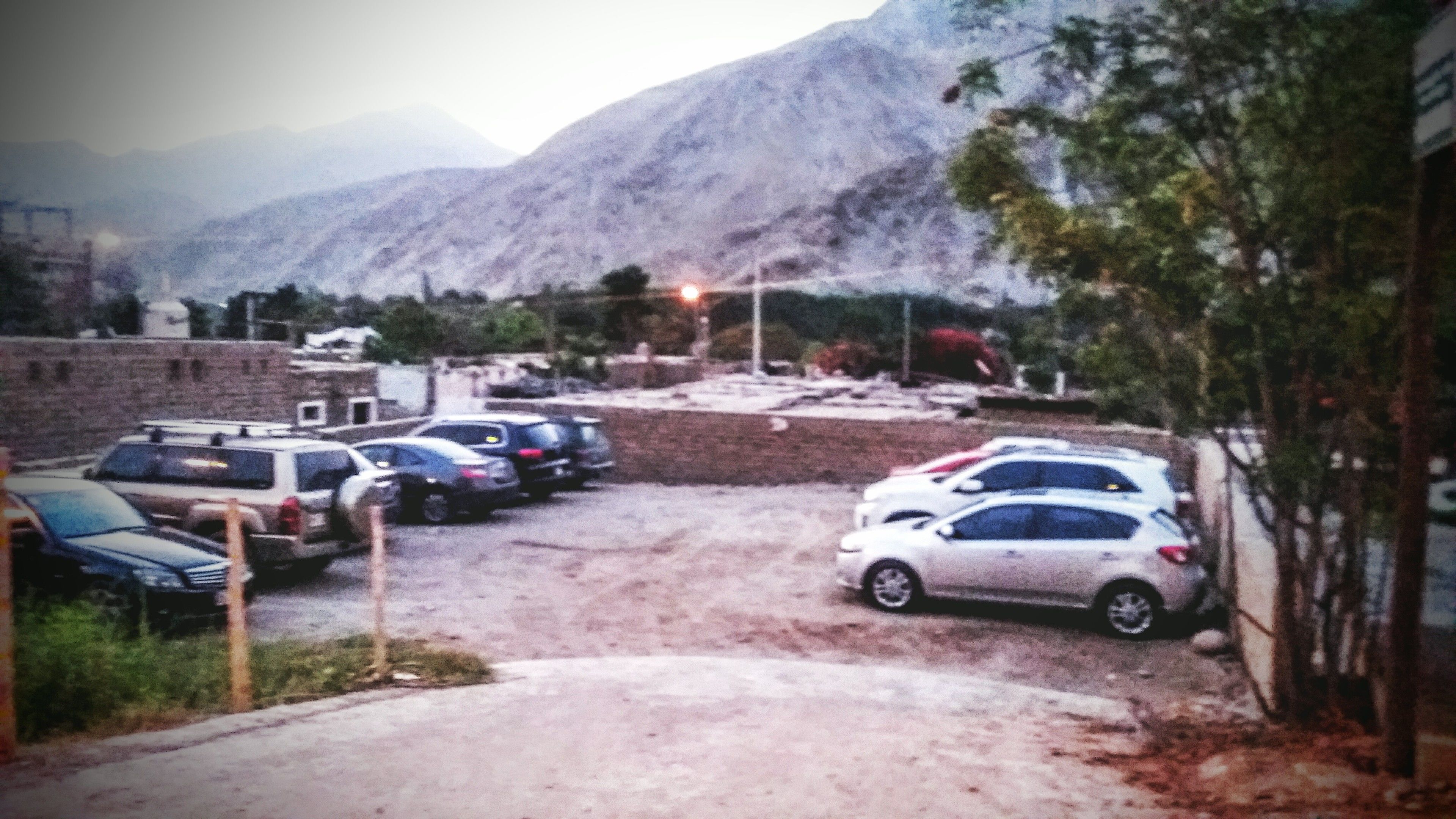 A parking area with several cars, a brick wall, and a mountain in the background.