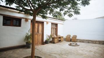 A courtyard with a tree, a wooden door, and wicker furniture.