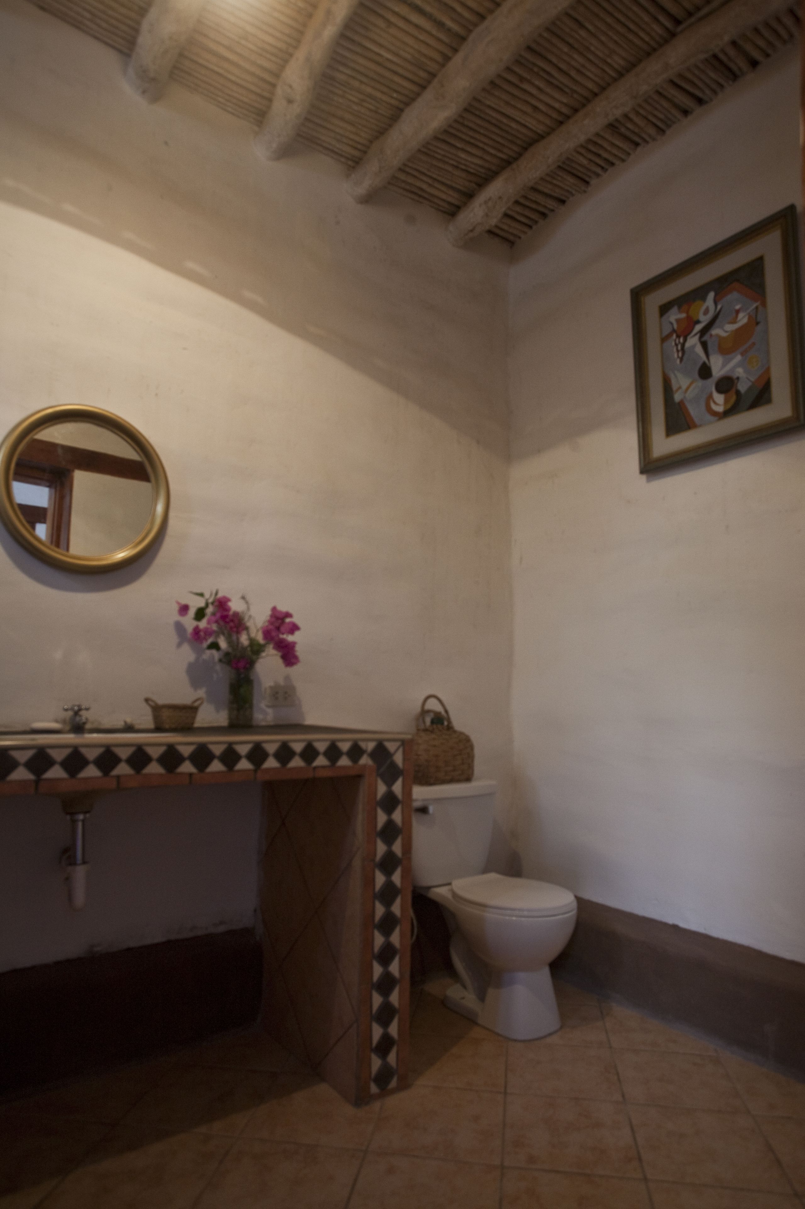 Une salle de bain avec un sol carrelé, un lavabo avec un miroir, des toilettes et une œuvre d’art encadrée au mur.