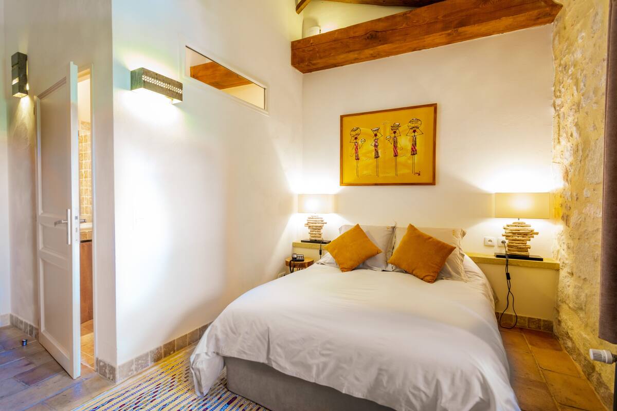 Un dormitorio con una cama grande, dos mesitas de noche con lámparas, un cuadro en la pared y una viga de techo de madera.