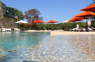 Piscina límpida com espreguiçadeiras e guarda-sóis, cercada por muros de pedra e árvores.