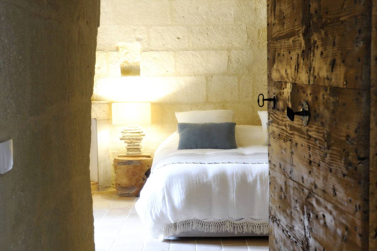 Un pasillo estrecho que conduce a un dormitorio con cama, mesita de noche y lámpara.