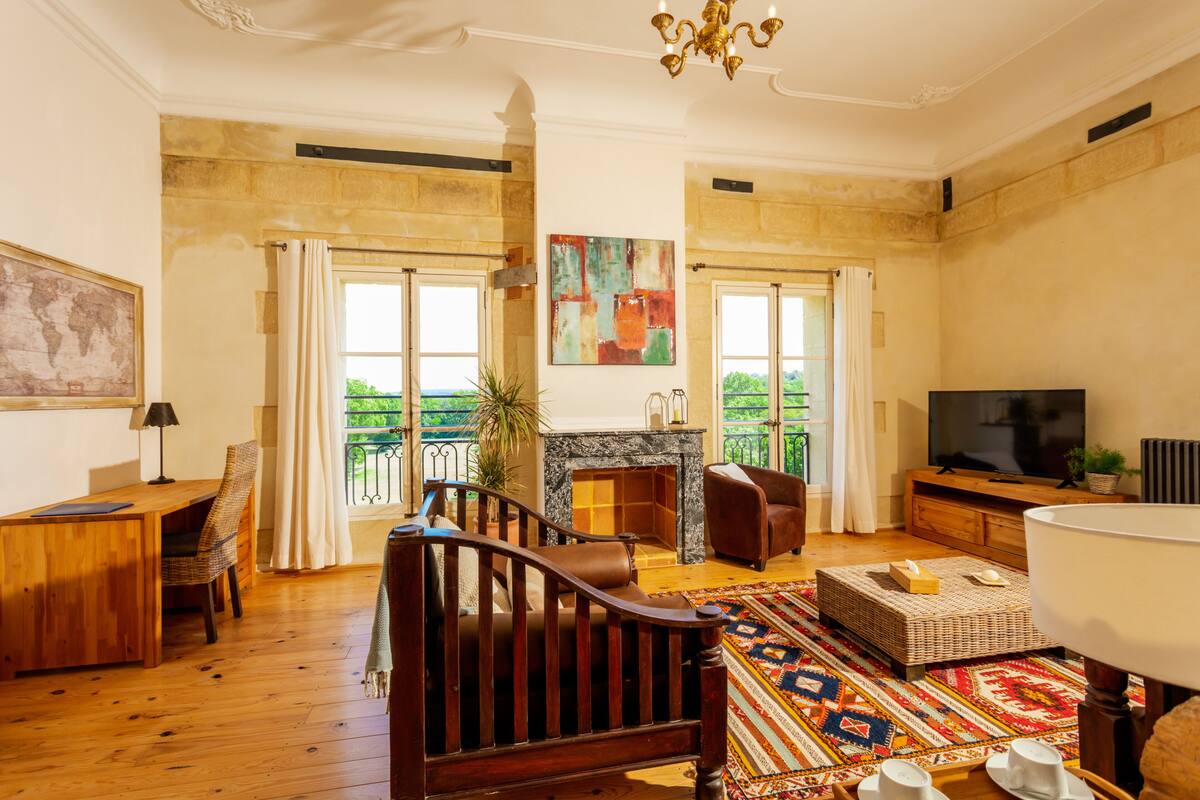 Un salón amplio con chimenea, muebles de madera, televisor y ventanas grandes que ofrecen vistas a la vegetación.