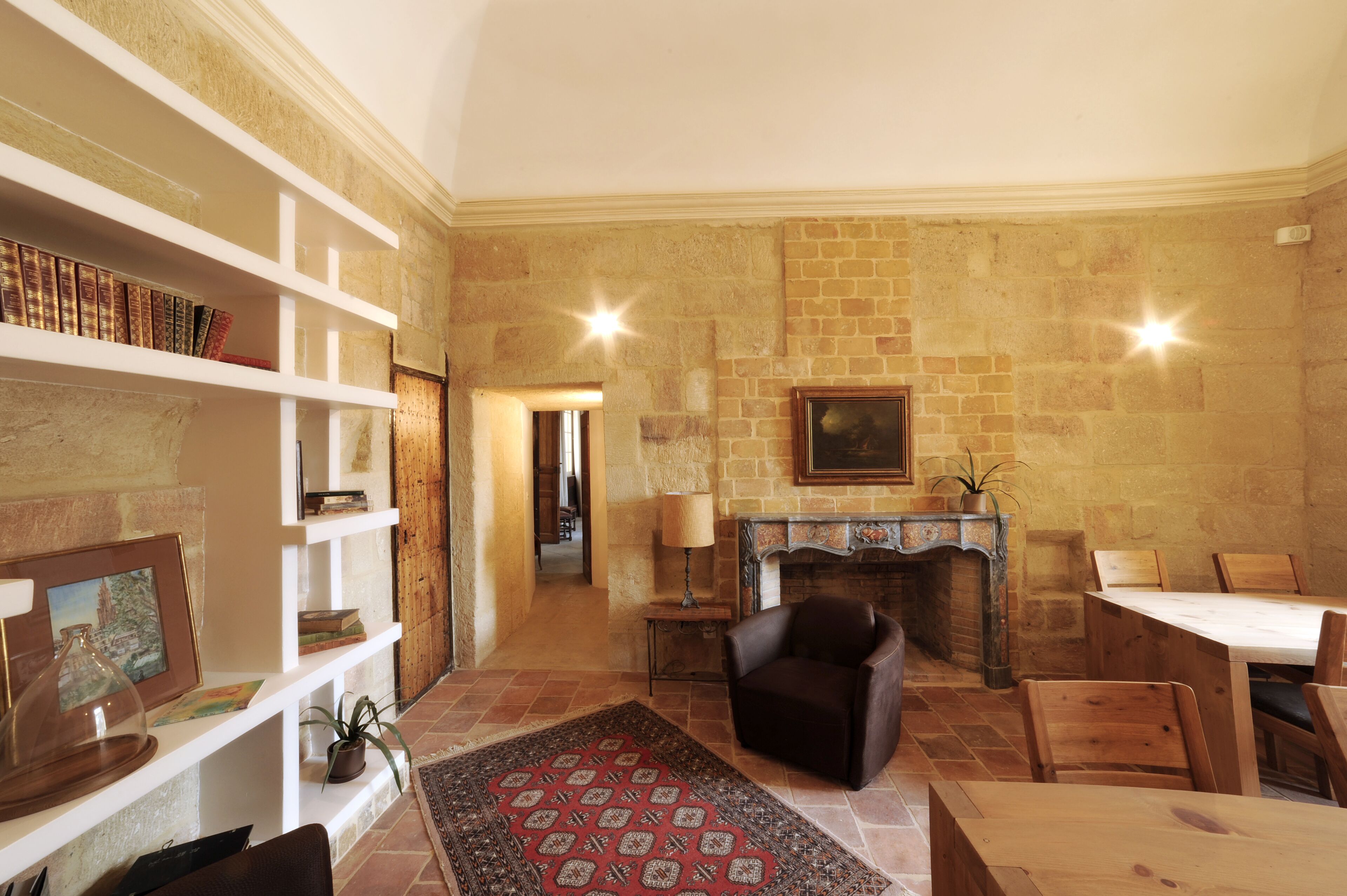 A cozy living room with a fireplace, a bookshelf, a dining area, and a patterned rug.