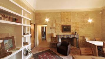 A cozy living room with a fireplace, a bookshelf, a dining area, and a patterned rug.