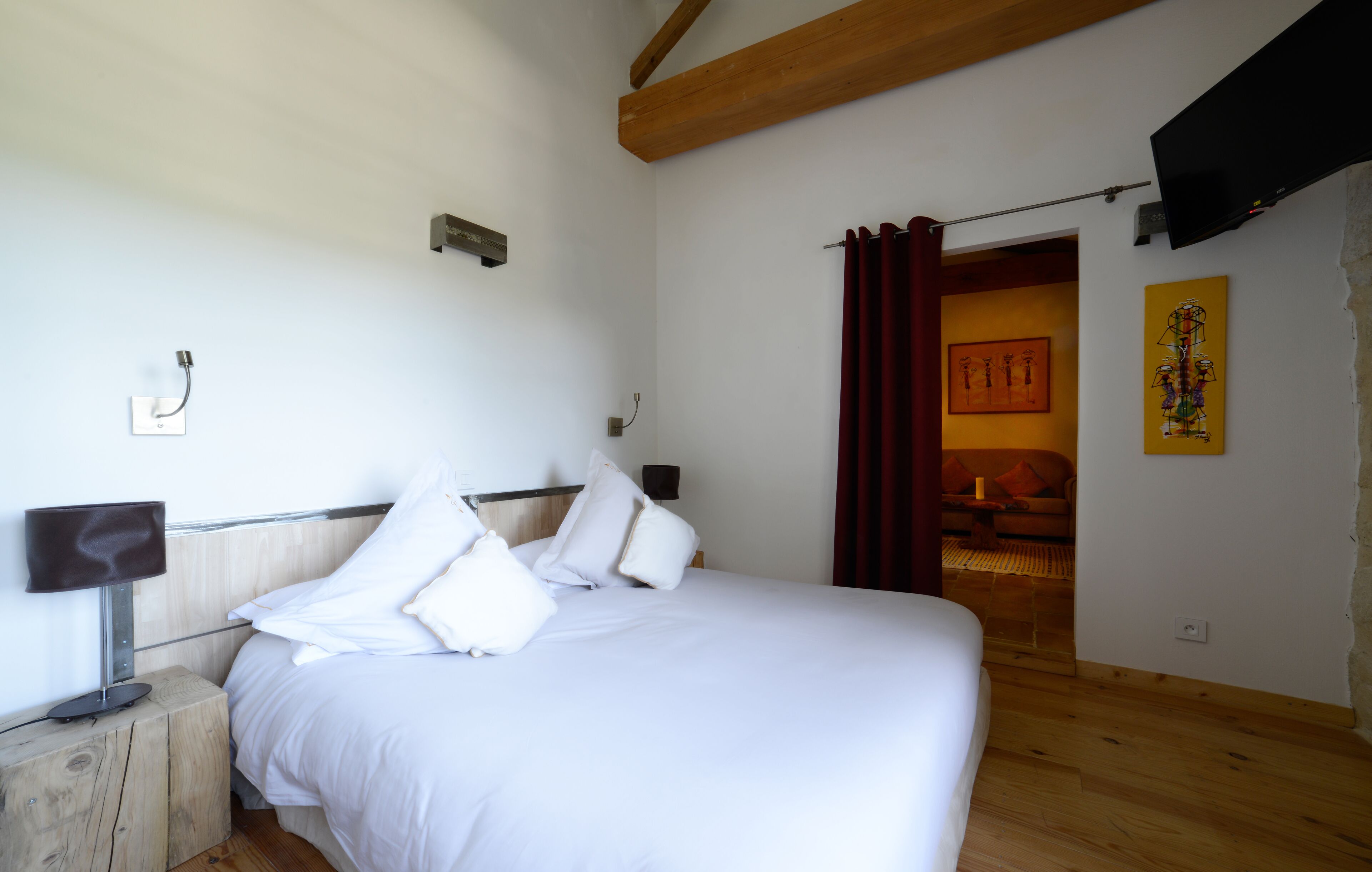 Een slaapkamer met een bed, een houten hoofdbord, een nachtkastje, een flatscreen televisie aan de muur en een deur naar een andere kamer.