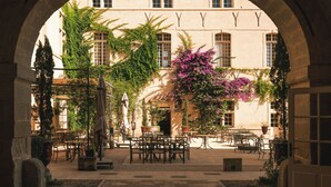 Un patio exterior con arcos de piedra, mesas, sillas y macetas con plantas.