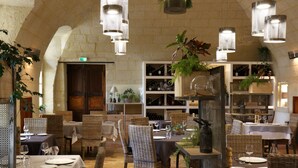 Un restaurante con techos altos, mobiliario de mimbre e iluminación colgante. Las mesas están dispuestas con manteles blancos y copas de vino.