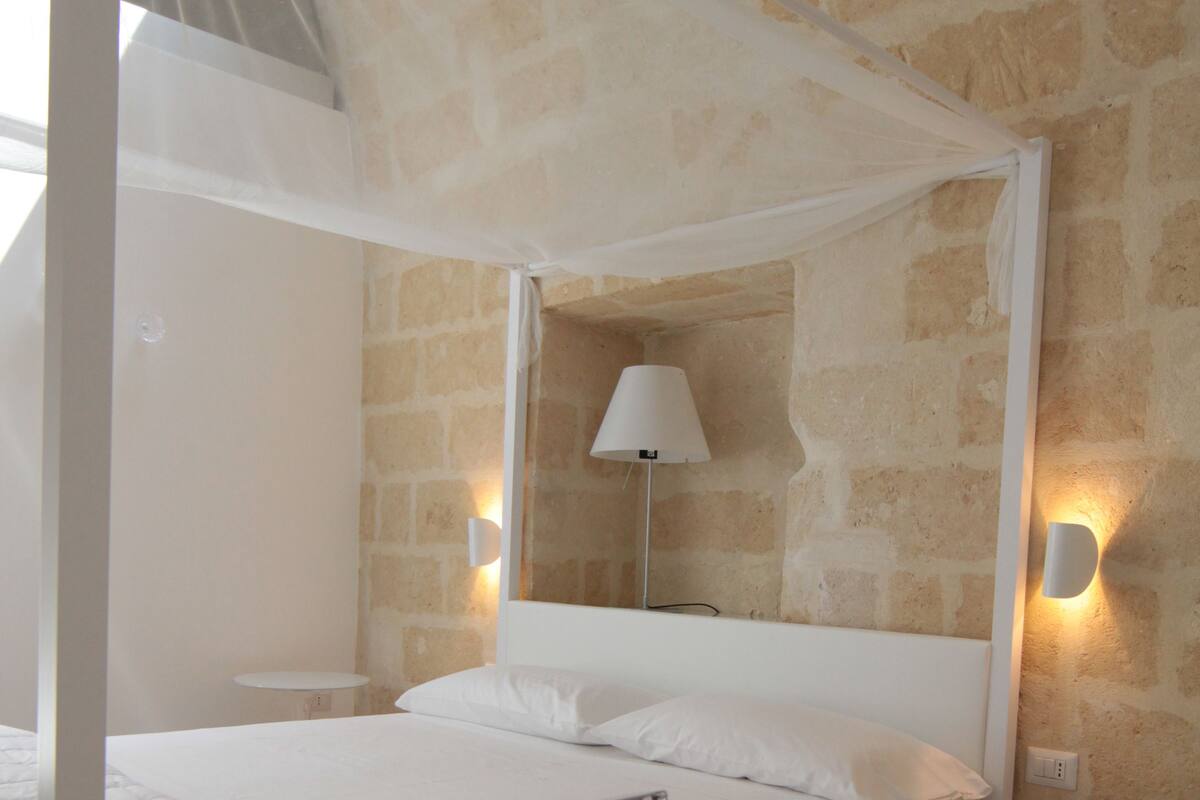 A bedroom with a four-poster bed, a stone wall, and two bedside lamps.