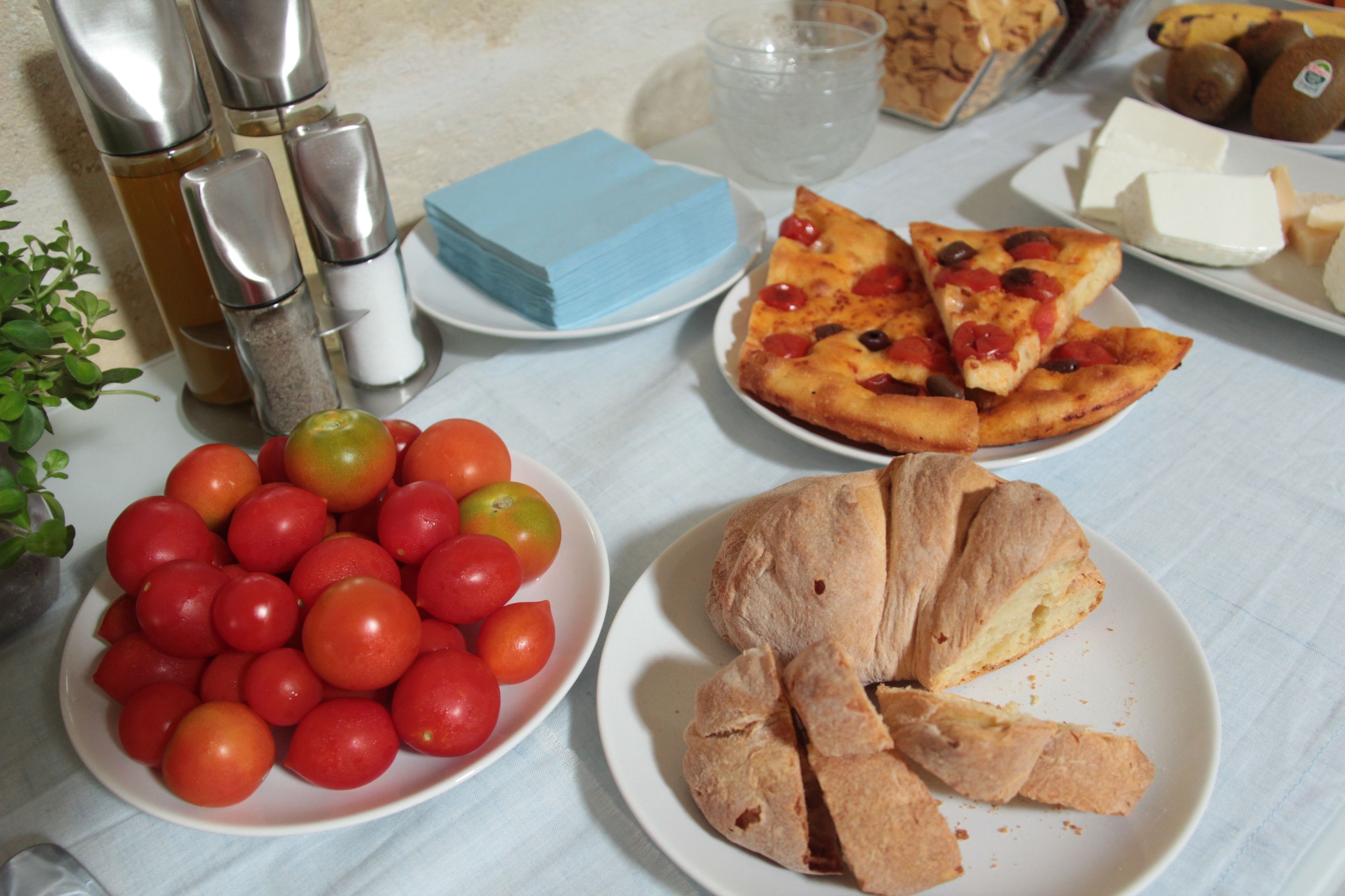 Una mesa con diversos alimentos, incluyendo tomates, pizza y pan.