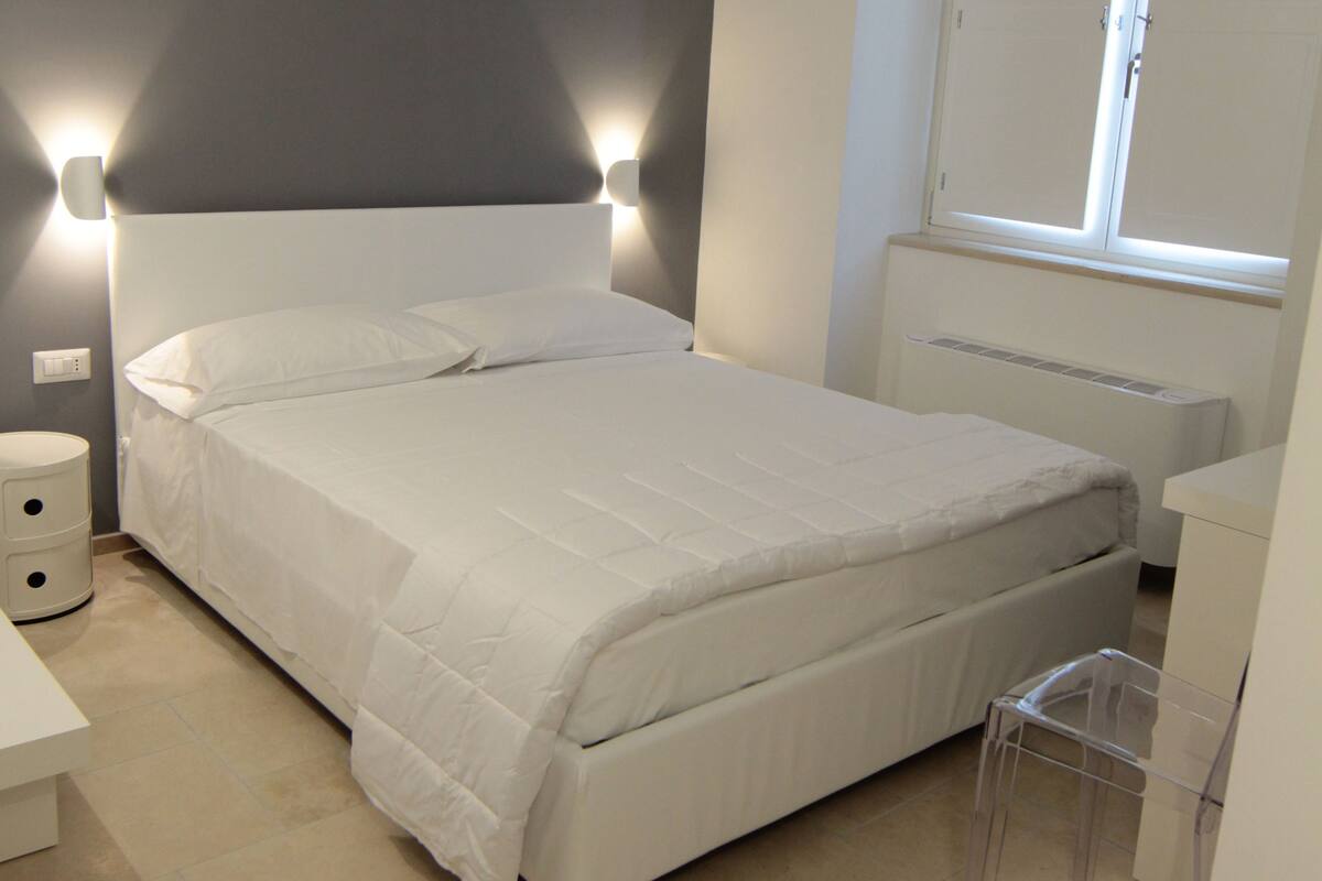 A bedroom with a bed, bedside table, and a window.