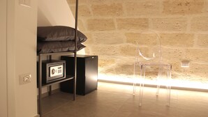 Un letto a castello con materasso, una piccola cassaforte nera e una sedia trasparente in plastica in una stanza con parete in pietra.