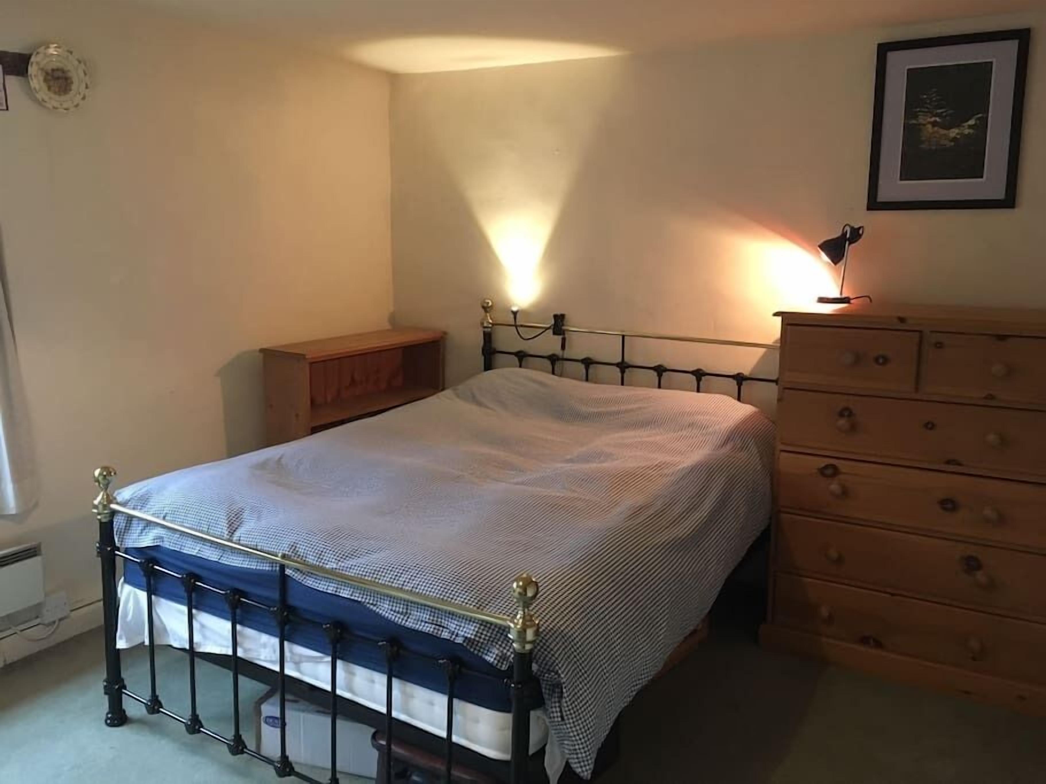 A bedroom with a bed, a wooden dresser, a nightstand, and a framed picture on the wall.