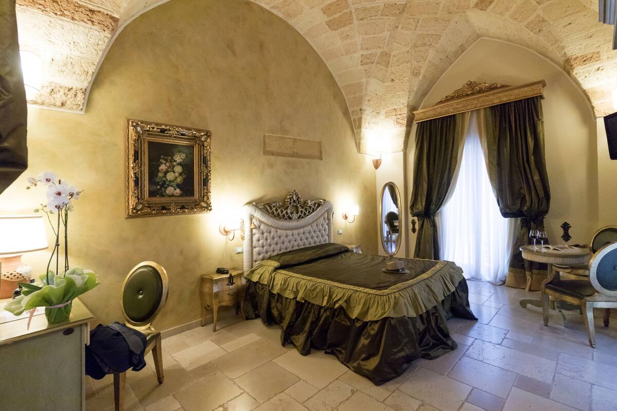 Een slaapkamer met een bed, een bureau, een stoel, een spiegel en een ingelijst schilderij aan de muur.
