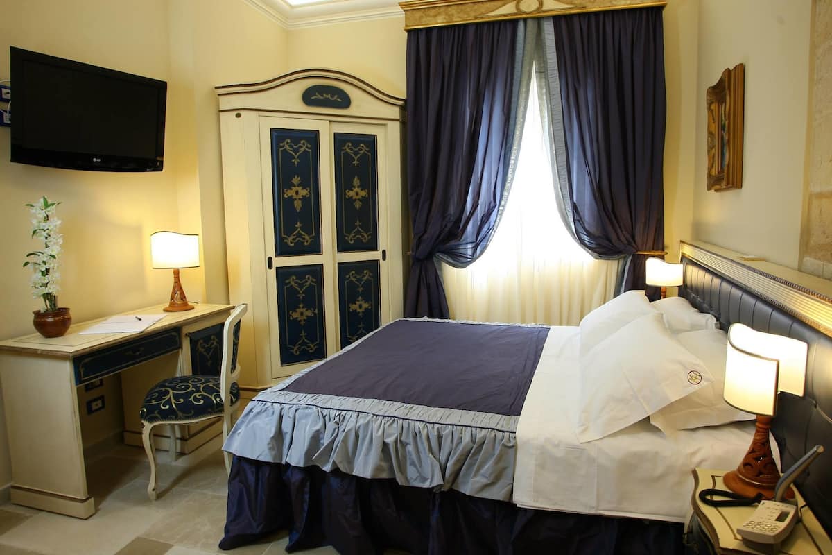 Een hotelkamer met een bed, bureau, stoel, televisie, gordijnen en een lamp.