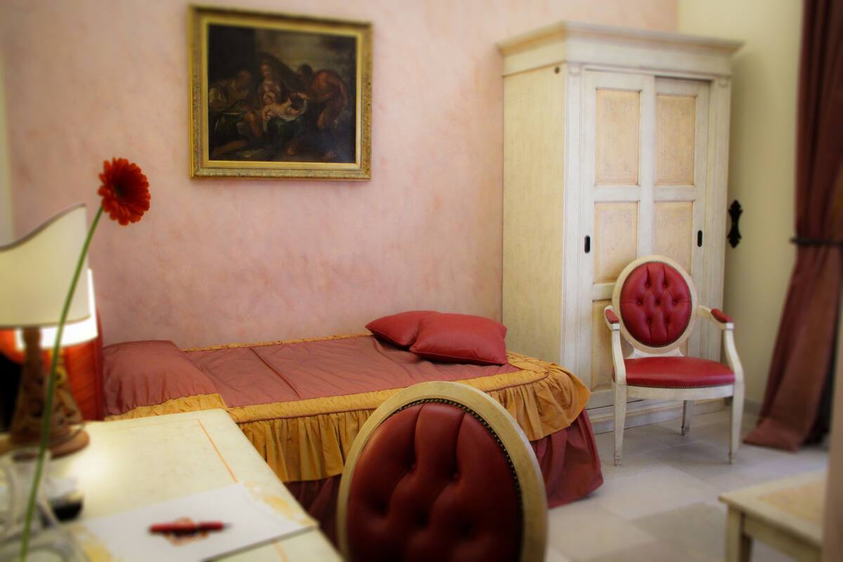 Een slaapkamer met een bed, een stoel, een kast en een schilderij aan de muur.