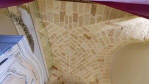 A stone vaulted ceiling with a central ventilation grate, a marble staircase, and a wall with a floral garland.