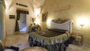 A bedroom with a large bed, a small table with wine glasses, a nightstand, and a staircase leading to another room.