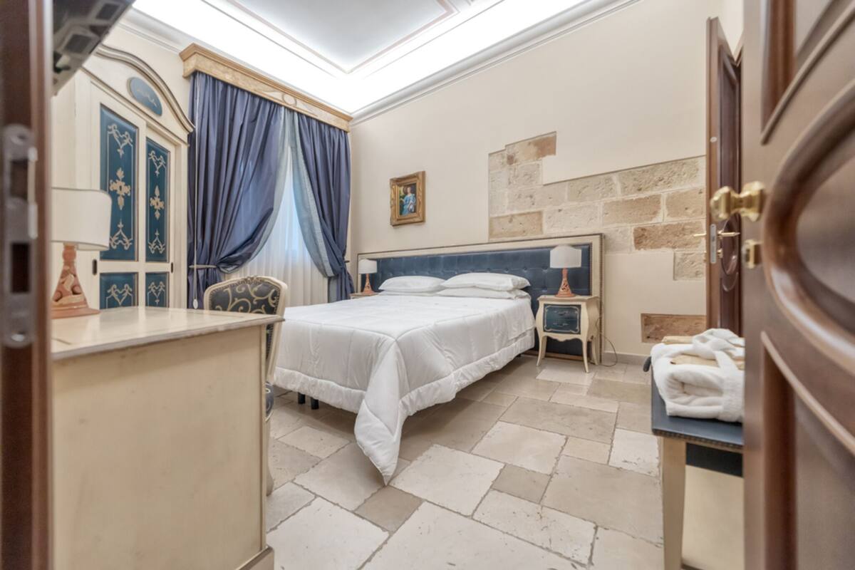 Een slaapkamer met een bed, nachtkastjes, een dressoir, een bureau en een stenen muur.