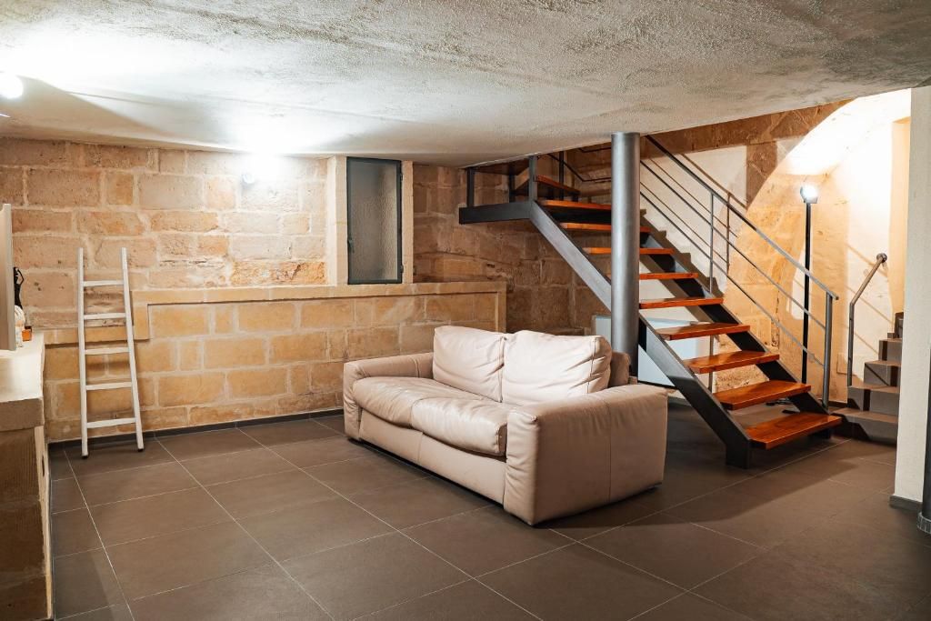 A room with a stone wall, a beige sofa, a staircase with wooden steps, and a metal railing.