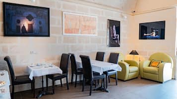 Un coin repas avec une table dressée pour deux personnes, un canapé et des œuvres d’art accrochées aux murs.
